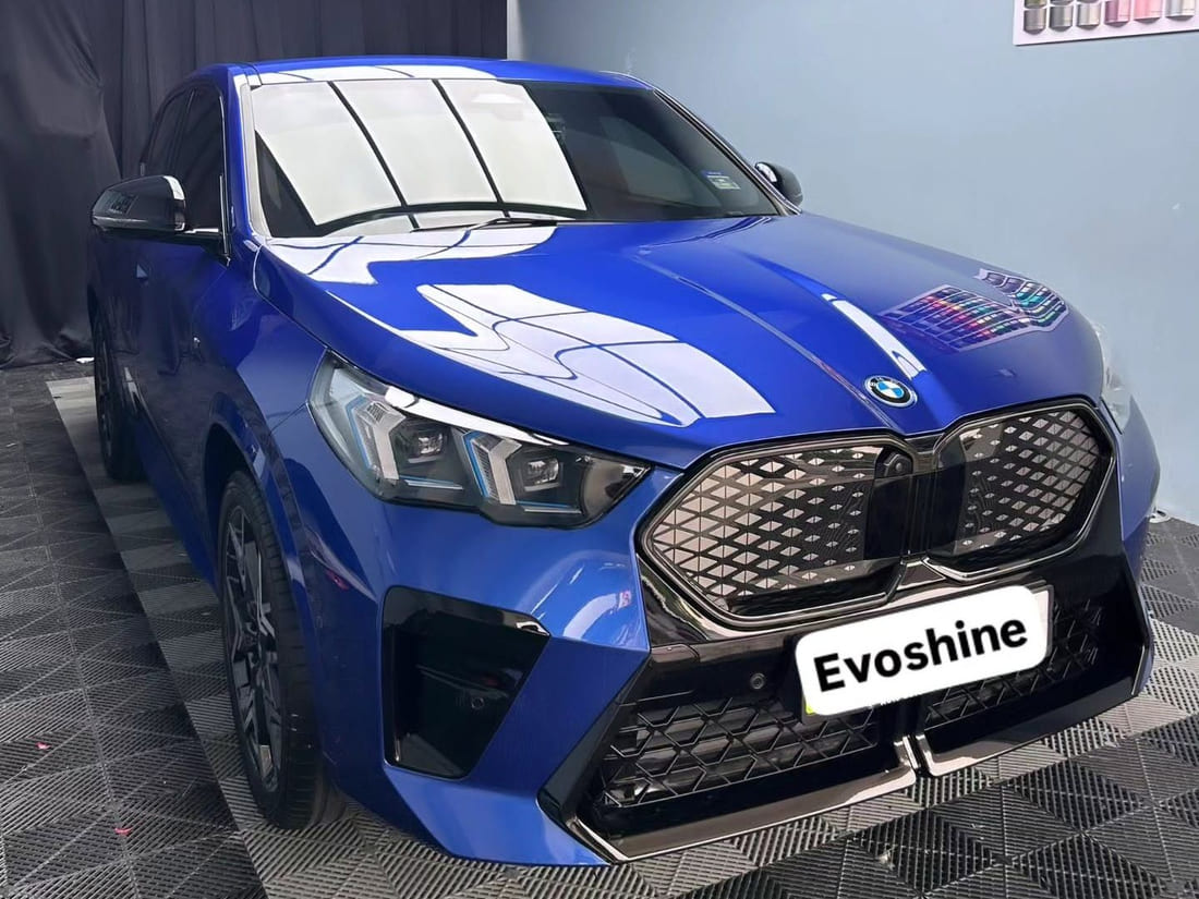 The enclosed Evo Shine Kajang bay: pale blue-grey walls, a black drape, a checker-plate floor and the workshop colour-wrap swatch chart, with a blue BMW iX2 standing in it.